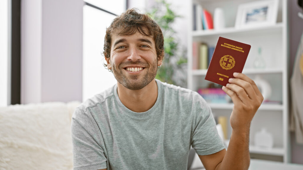 Learn Greek Hub delighted young man, a beaming passport holder passes the day in his cozy home, joyously sitting on the sofa embracing his greece heritage.